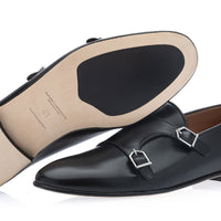 A pair of black leather double monk loafers shown on a white background, with one shoe positioned to display the tan insole and the other showing the side profile with silver-tone buckle details. | Image 2