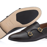 A pair of cocoa leather double monk loafers with gold buckle details, shown on a white background with one shoe displaying the sole. | Image 2