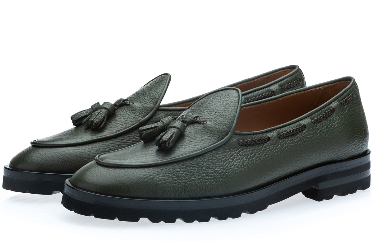 A pair of dark musk green pebbled leather loafers with decorative tassels on the vamp and thick black lug soles, shown on a clean white background.