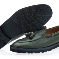 An musk green pebbled leather loafer with a tassel detail, shown alongside its black treaded outsole on a white background. | Image 2