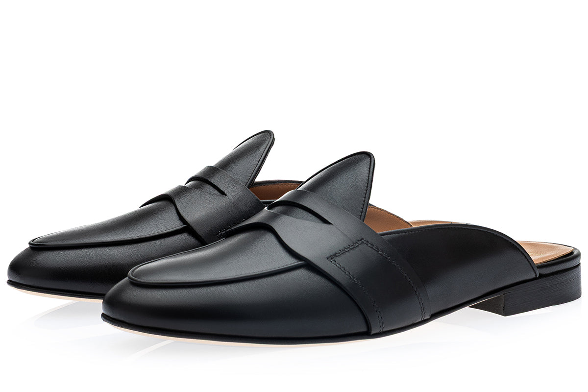A pair of black leather penny loafer mule slides with a low block heel, displayed on a clean white background.