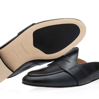 A pair of black leather slip-on mule loafers shown on a white background, with one shoe angled to display the beige insole and the other showing the side profile. | Image 2