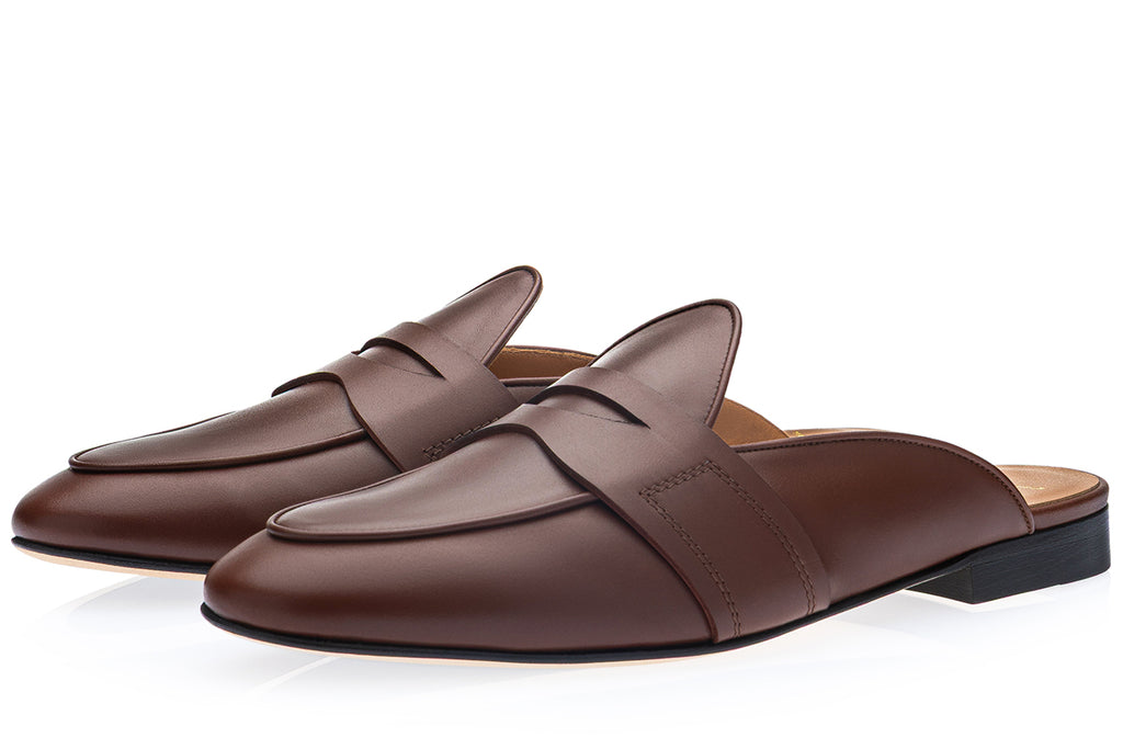 A pair of dark brown cognac leather mule loafers with a wide decorative strap across the vamp, shown on a clean white background.